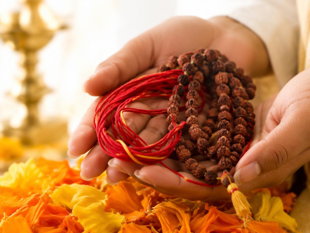 Hands holding a red sacred thread and rudraksha mala over flower petals